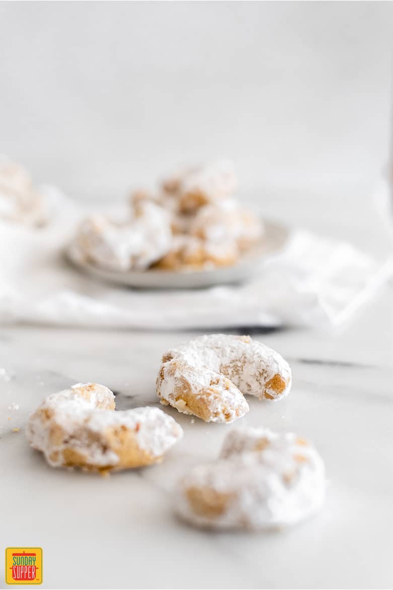 Three Greek wedding cookies with a plate of cookies in the background