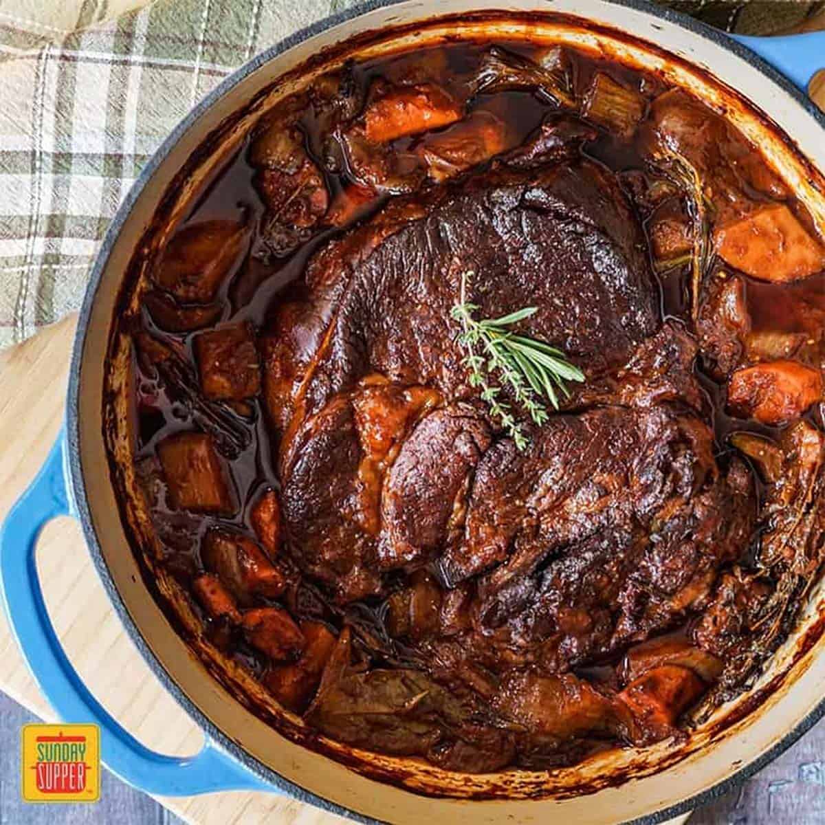 Overhead shot of the beef chuck roast recipe in a blue dutch oven with fresh herbs on top