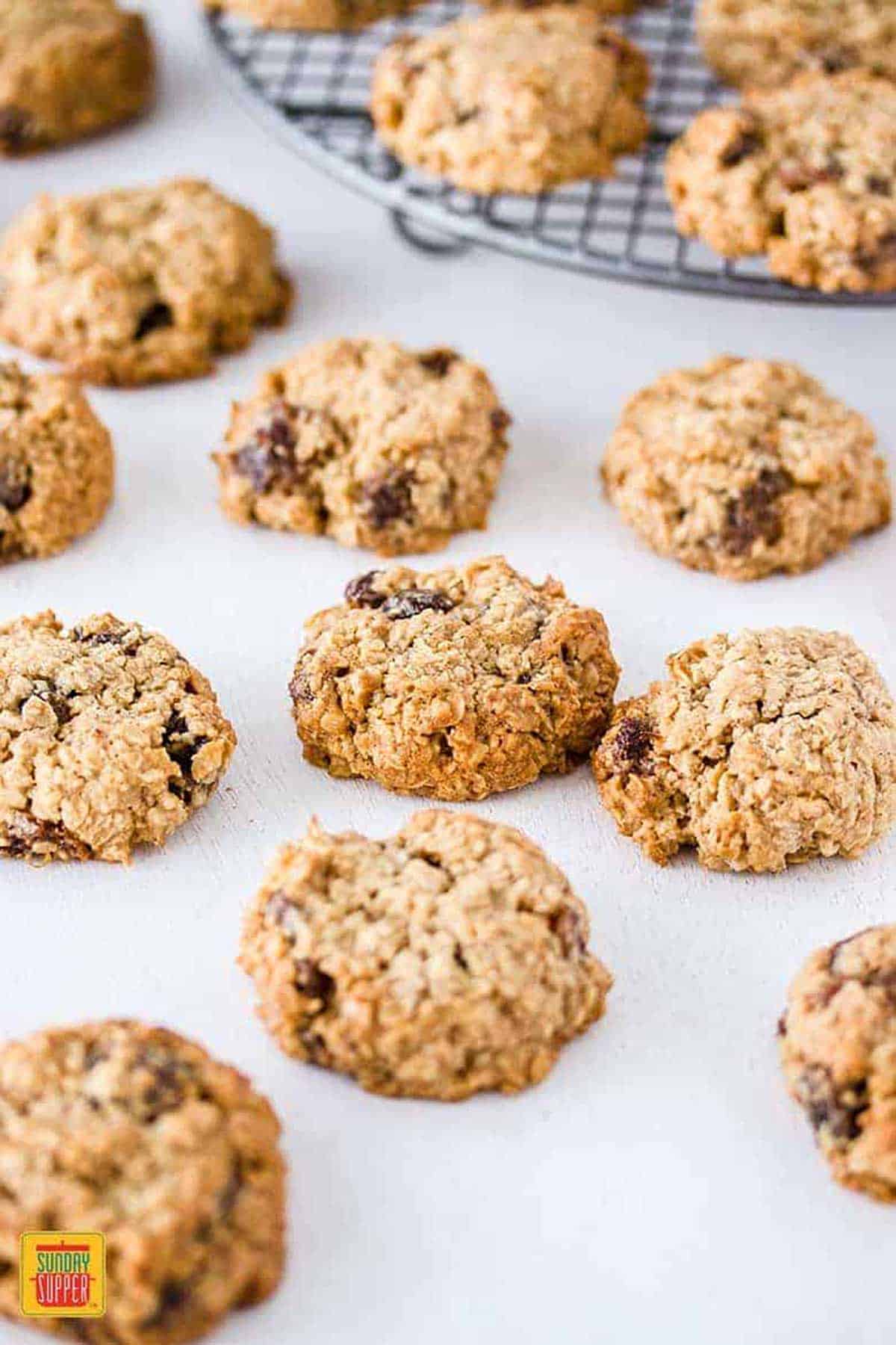 Oatmeal raisin cookies on a white surface, some on a metal rack