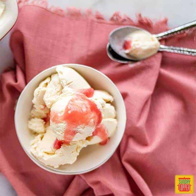 Rhubarb ice cream in a white dish with rhubarb sauce on top and two spoons nearby