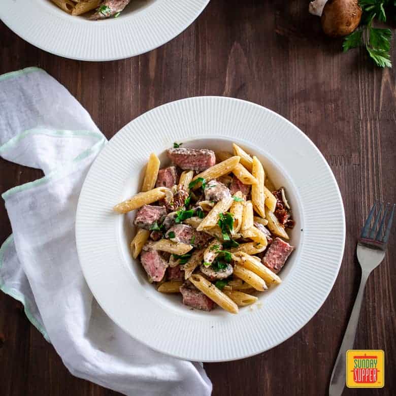  Creamy Penne Pasta with Sliced Prime Rib Served on a white plate with a fork