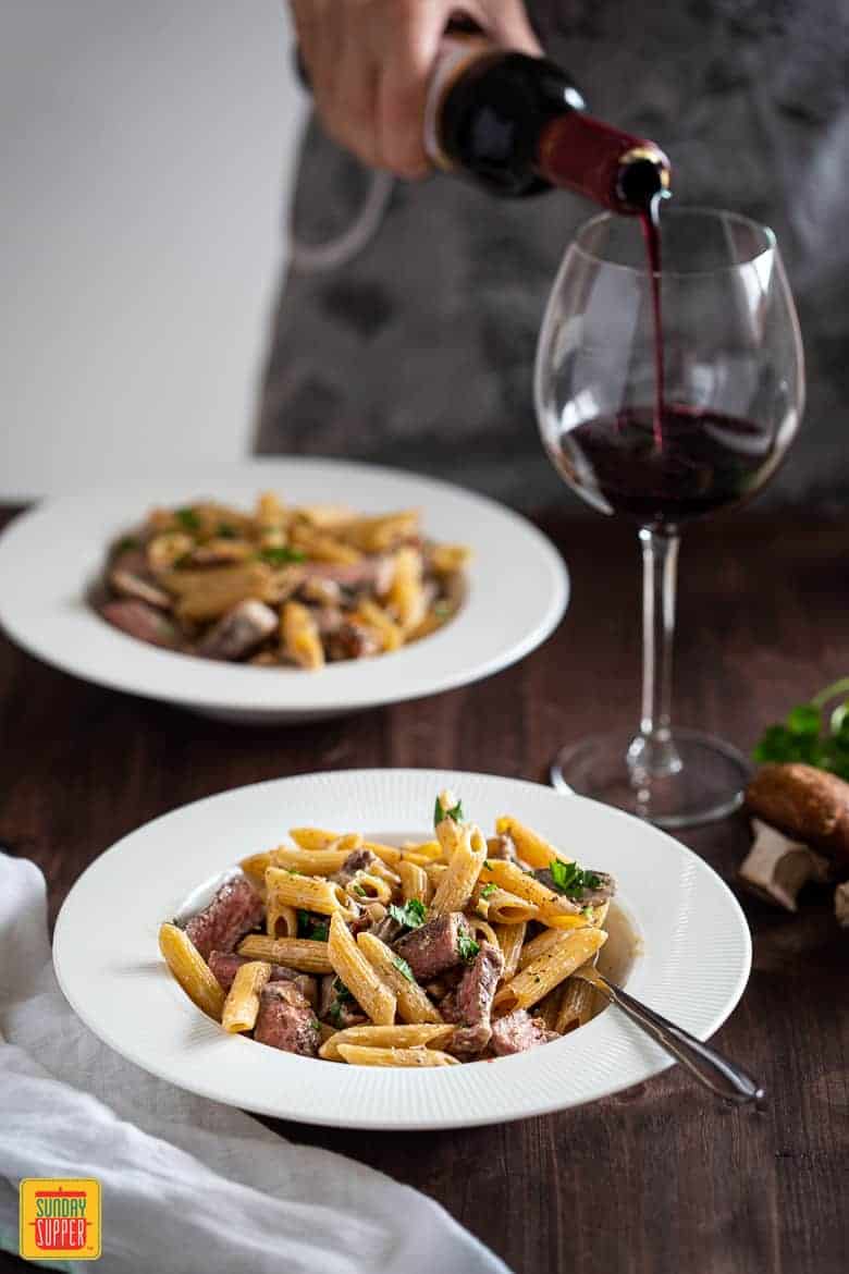 Creamy Penne Pasta with Sliced Prime Rib served in a plate with wine being poured on the side