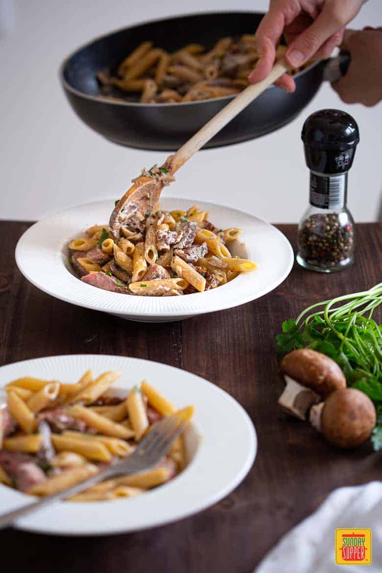 Creamy Penne Pasta with Sliced Prime Rib being served in a plate on a wooden table