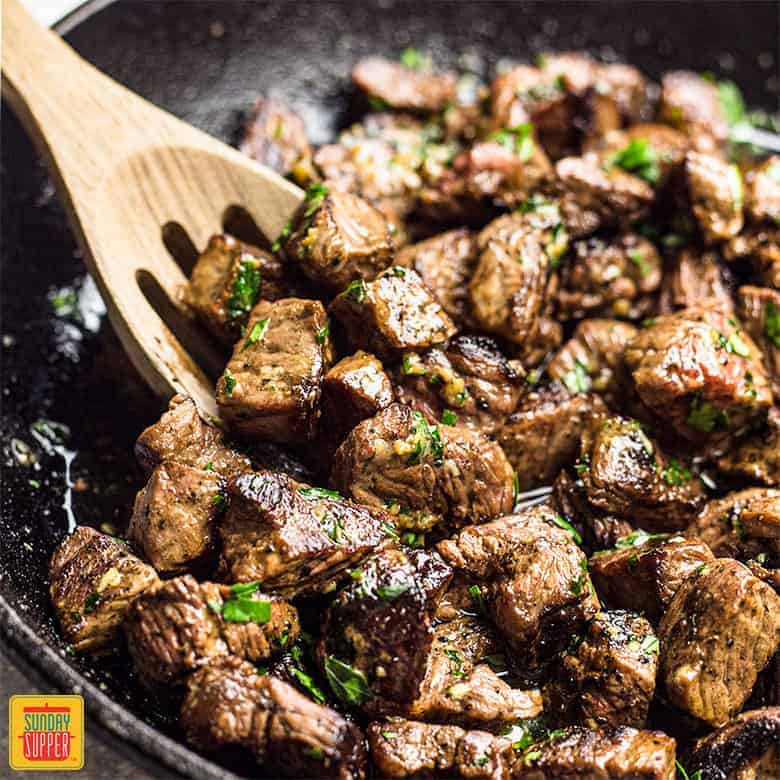 garlic butter steak bites in a black skillet with a wooden slotted spoon