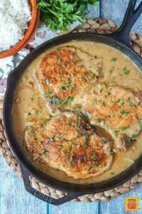 Smothered Pork Chops in a cast iron pan with rice and parsley
