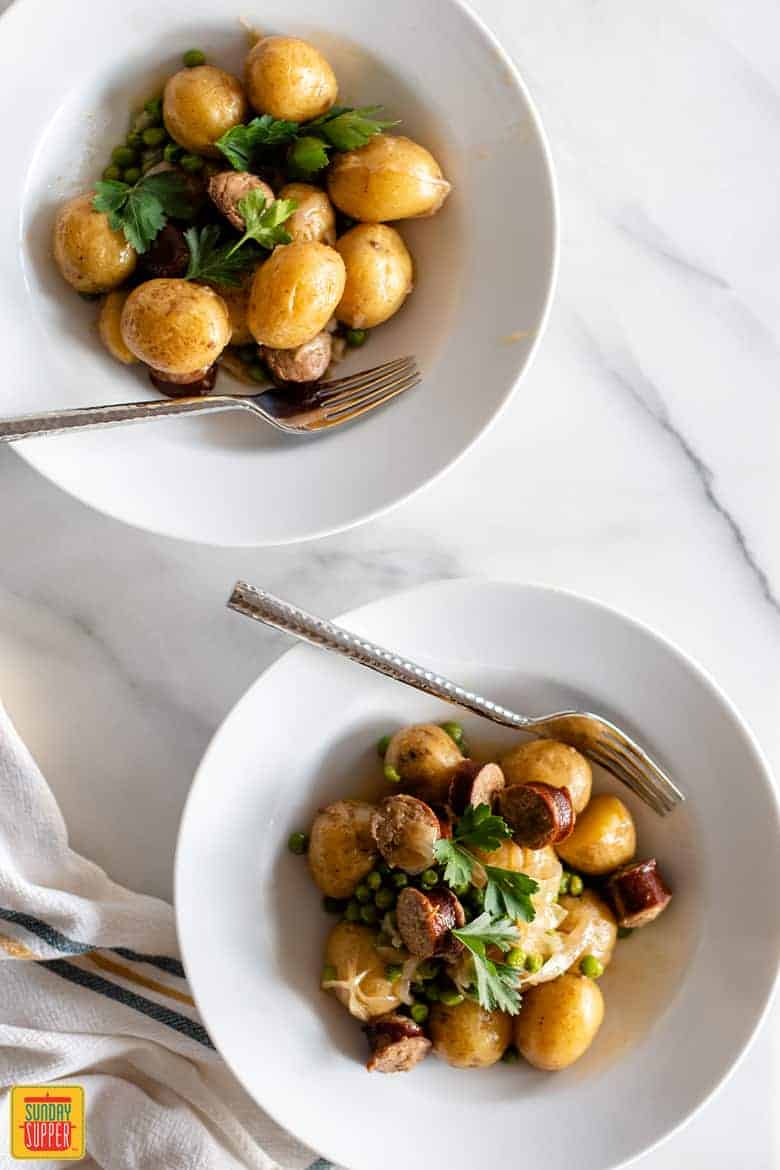 Smothered potatoes and sausage in white bowls with forks