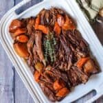 Overhead shot of beef chuck roast recipe on a white platter with carrots and fresh herbs