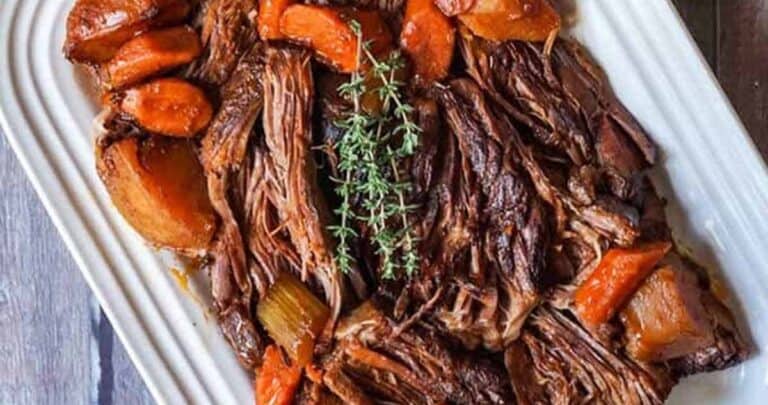 Overhead shot of beef chuck roast recipe on a white platter with carrots and fresh herbs