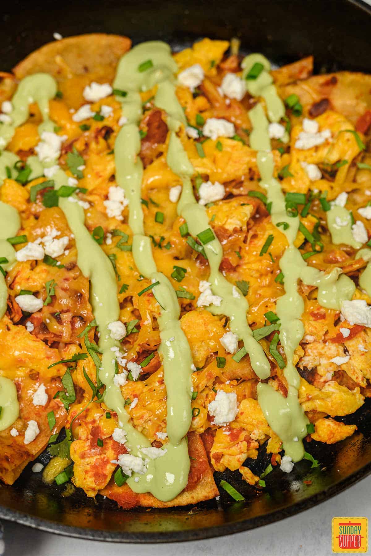 Close up of chilaquiles rojos in a cast iron skillet with avocado crema drizzled on top