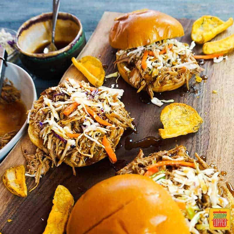 How to make pulled pork: Three pulled pork sandwiches with coleslaw on a cutting board with potato wedges