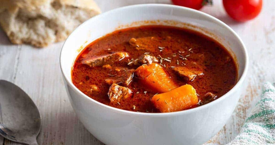 Instant pot Beef stew in a white bowl with a piece of bread and tomatoes