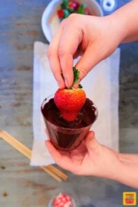 Dipping a strawberry into chocolate by holding it by the leaves