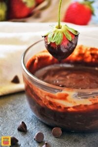 A strawberry dipped in ganache dripping into bowl of ganache
