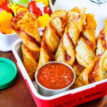 Puff pastry pizza twists in a bento box with marinara dipping sauce in a metal cup