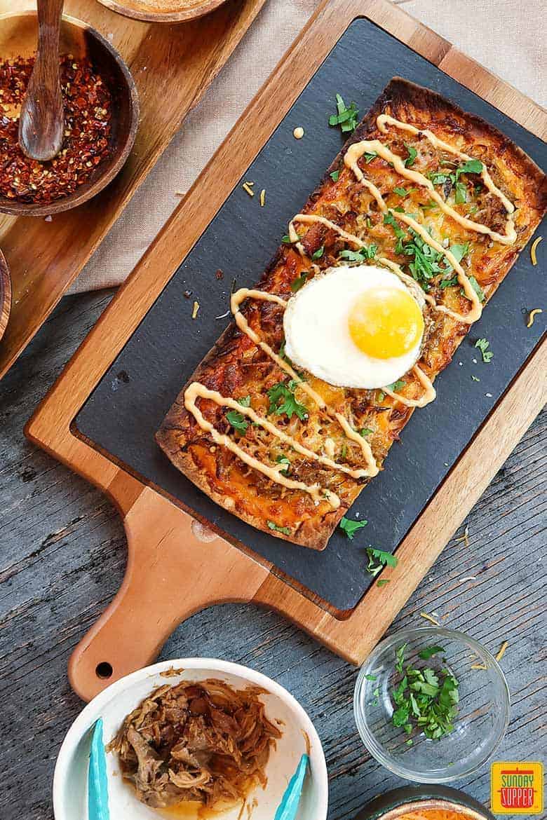 Slow cooker pulled pork pizza flatbread on black serving board with egg on top