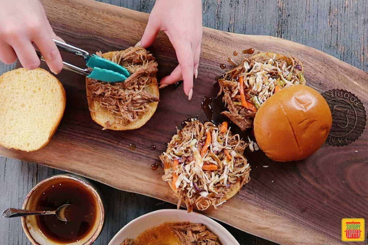 Using tongs to add pulled pork to a sandwich bun for pulled pork sandwich recipe