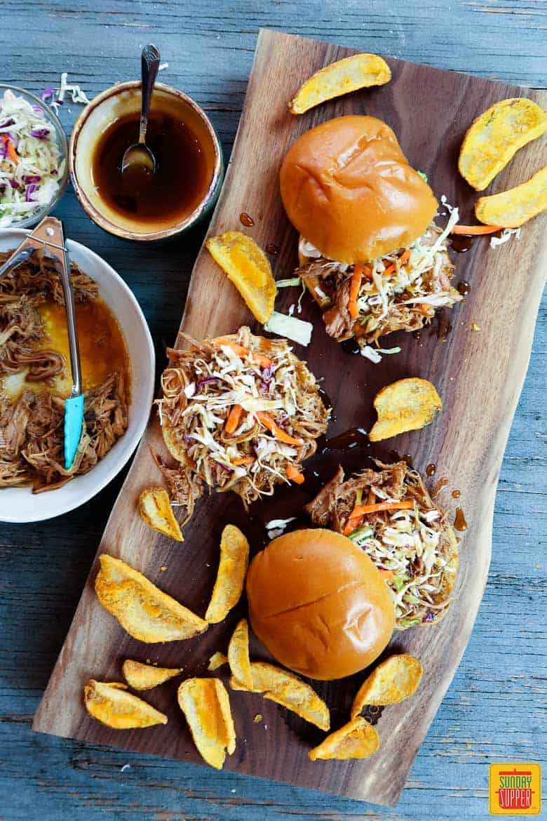 Three pulled pork sandwiches on a cutting board with slaw and extra pork