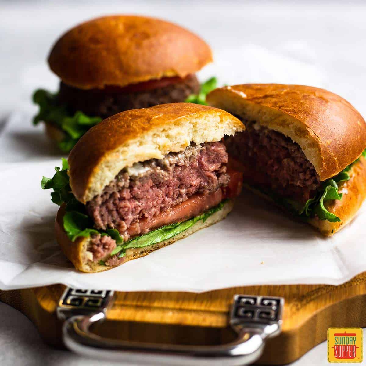 Air fryer burger with garlic butter spread cut in half on a piece of parchment paper over a wooden serving board