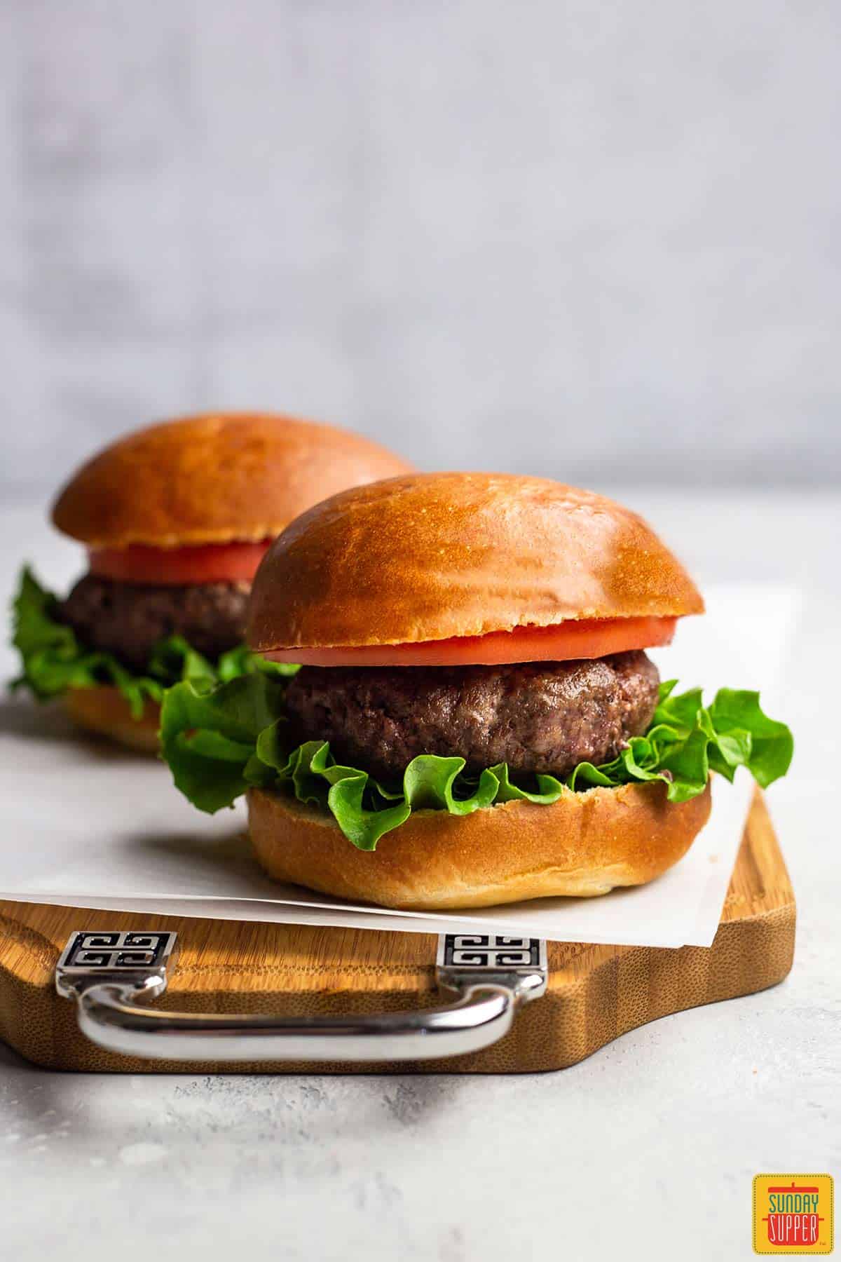 Two air fryer hamburgers on a piece of parchment paper over a wooden serving board