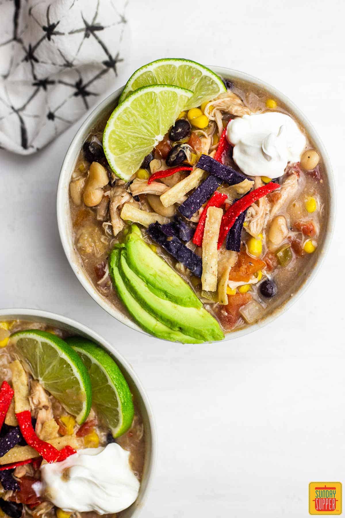 Two bowls of creamy shredded chicken tortilla soup with fresh limes and avocado