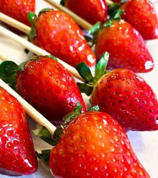 Two rows of nine candied strawberries on skewers over parchment paper