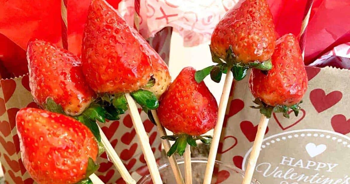 Six candied strawberries on skewers in front of Valentine's Day gift bags