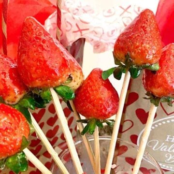 Six candied strawberries on skewers in front of Valentine's Day gift bags