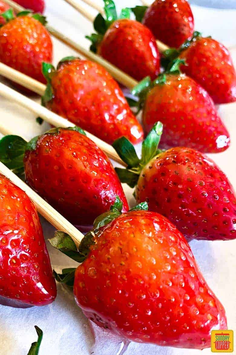 Two rows of nine candied strawberries on skewers over parchment paper