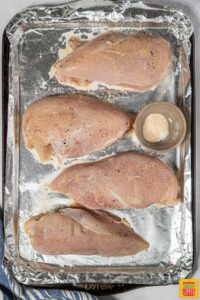 Four seasoned chicken breasts on a baking sheet lined with foil