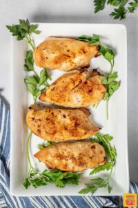 Four buttermilk roast chicken breasts on a white platter with herbs