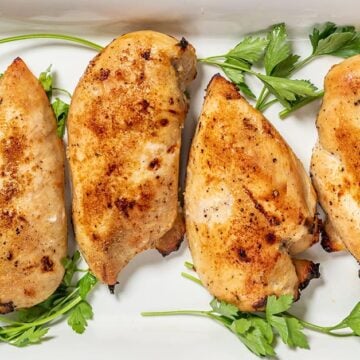 Four buttermilk roast chicken breasts on a white platter with herbs