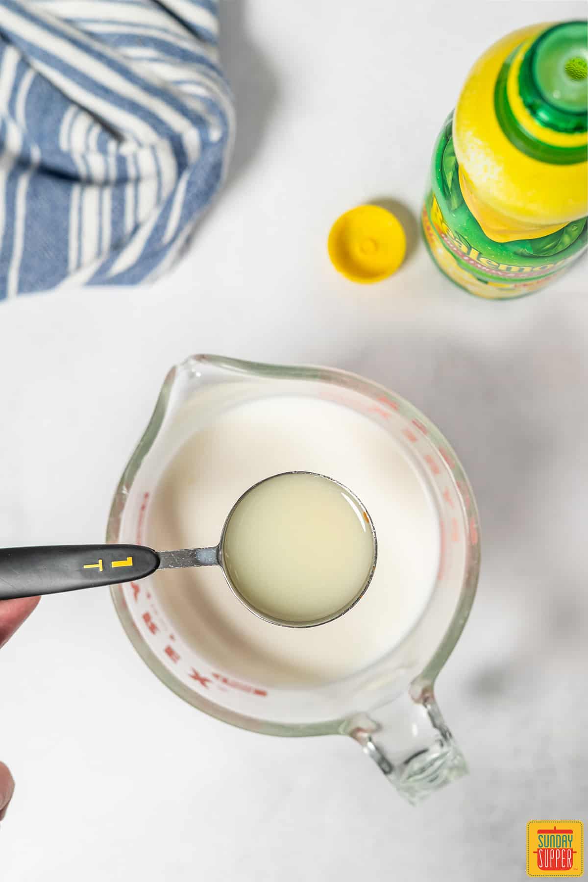 Lemon juice in a measuring spoon over a measuring cup of milk