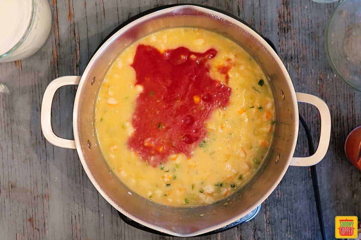 Adding tomato sauce to shrimp bisque recipe in pot