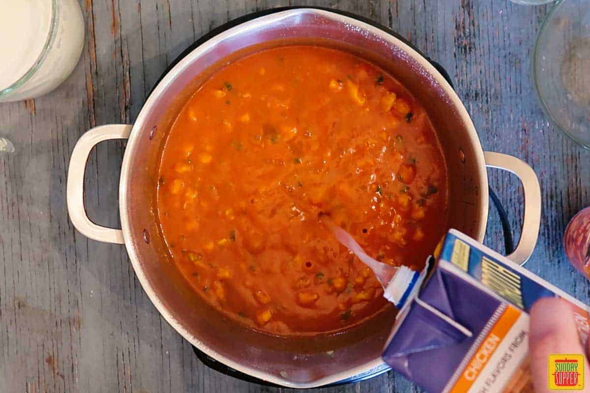 Adding chicken stock to shrimp bisque recipe in pot