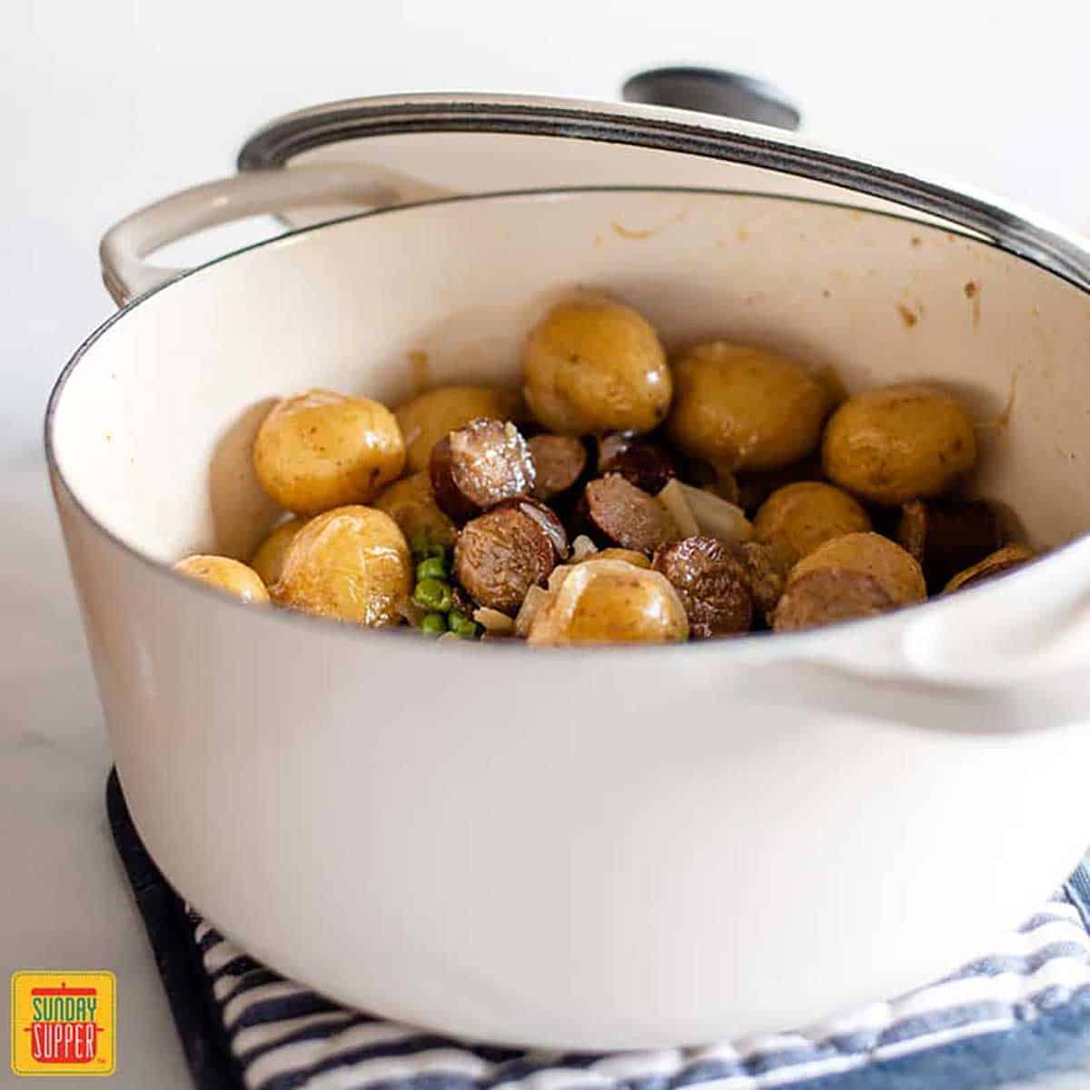 smothered potatoes and sausage in a white dutch oven with a lid