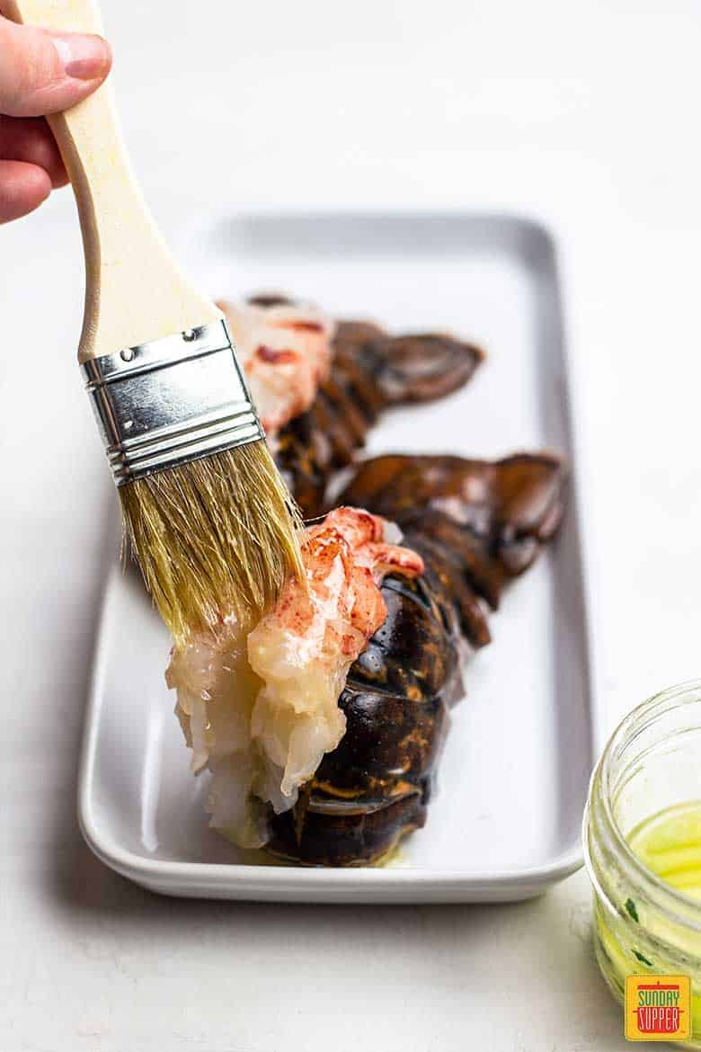 Brushing garlic butter onto lobster tails for air fryer surf and turf recipe
