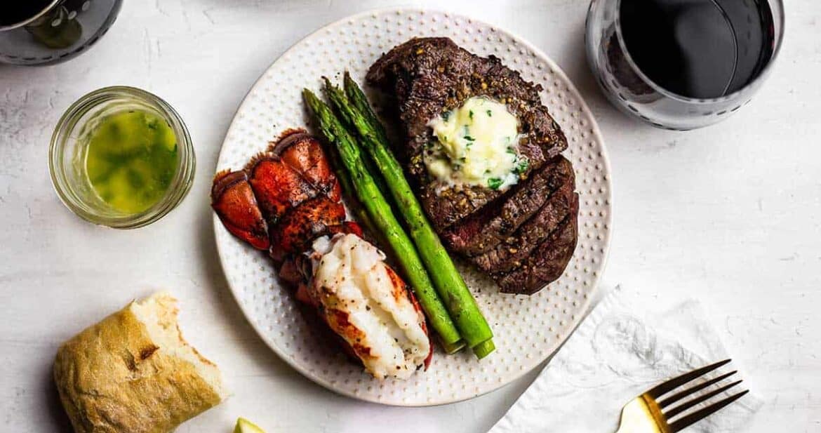 Plate with air fried steak and fried lobster tail with a side of steamed asparagus and a glass of wine