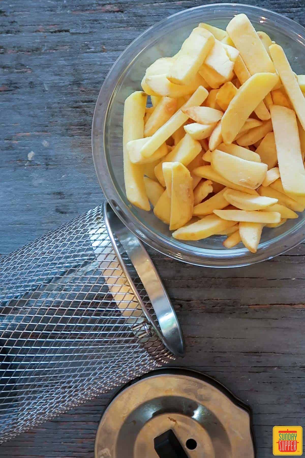 Air fryer basket and frozen French fries on a table