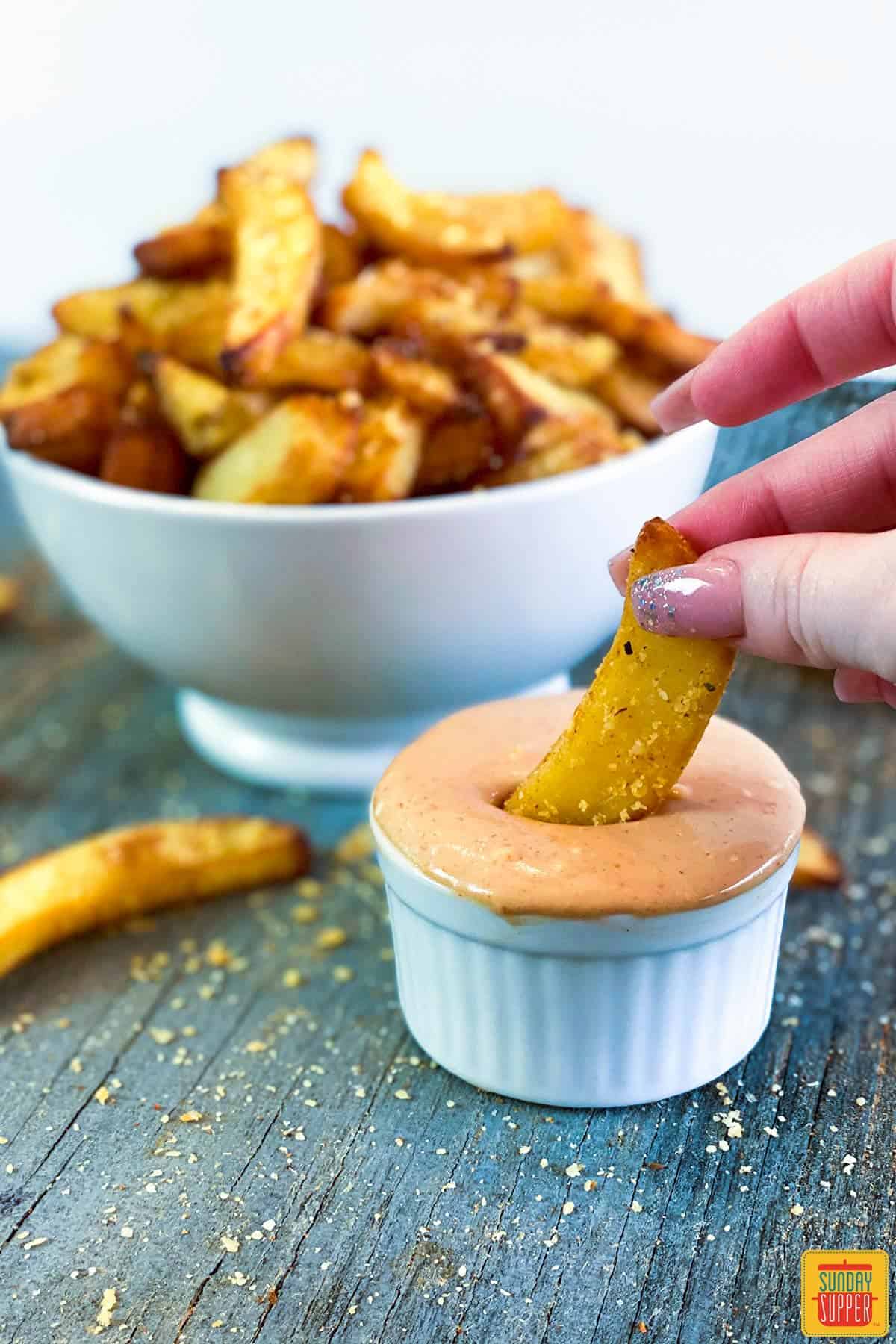 Dipping a fry in fry sauce in a white ramekin