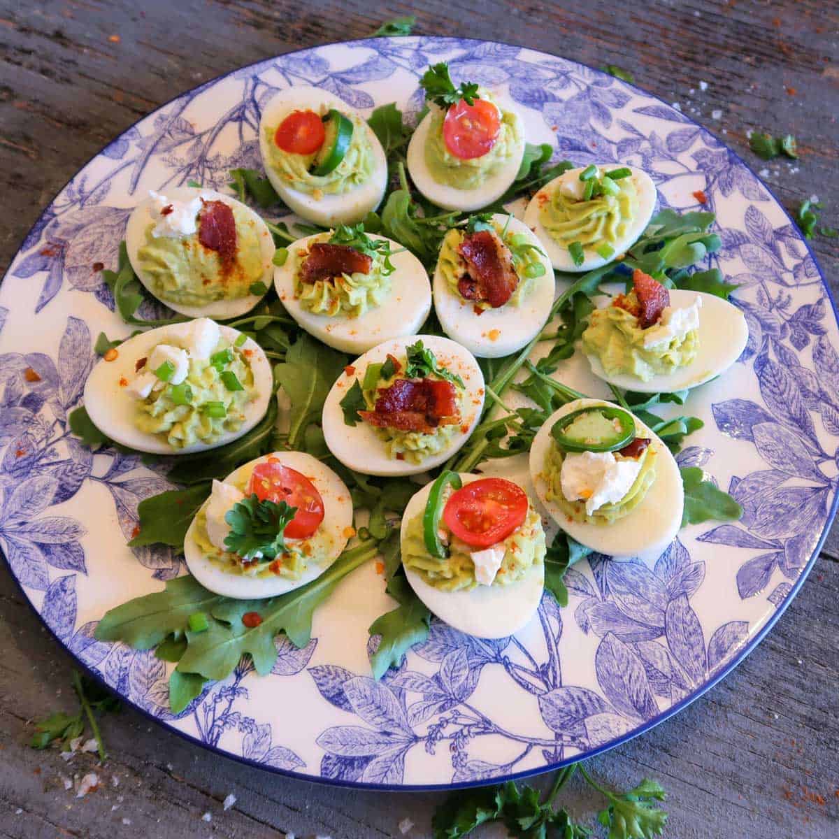 Close up of Avocado deviled eggs over a bed of greens on a white and blue floral plate