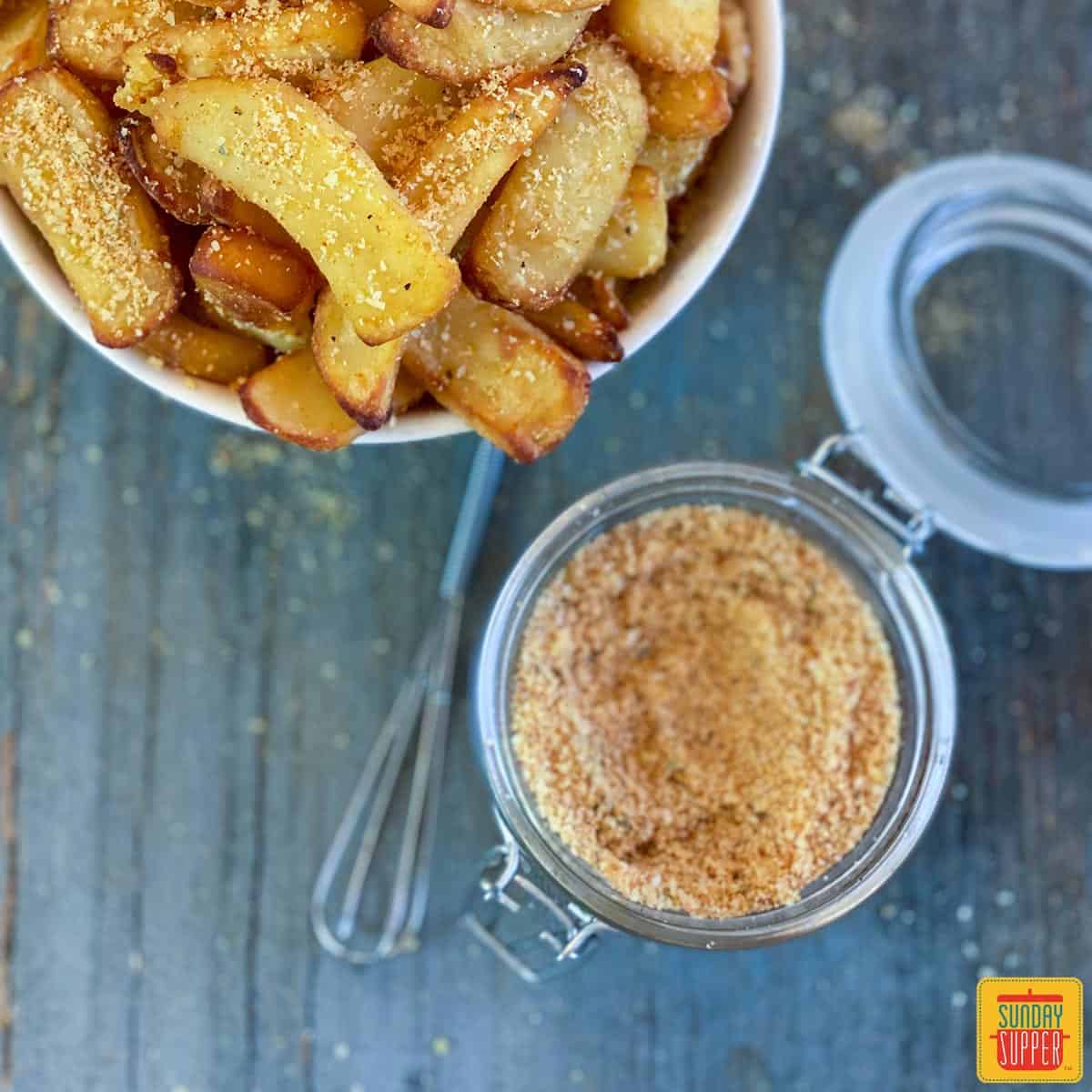 French fry seasoning in a jar next to air fryer fries in a bowl, perfect for using in gourmet burger recipees