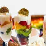 Three yogurt parfait glasses in front of rainbow charcuterie board