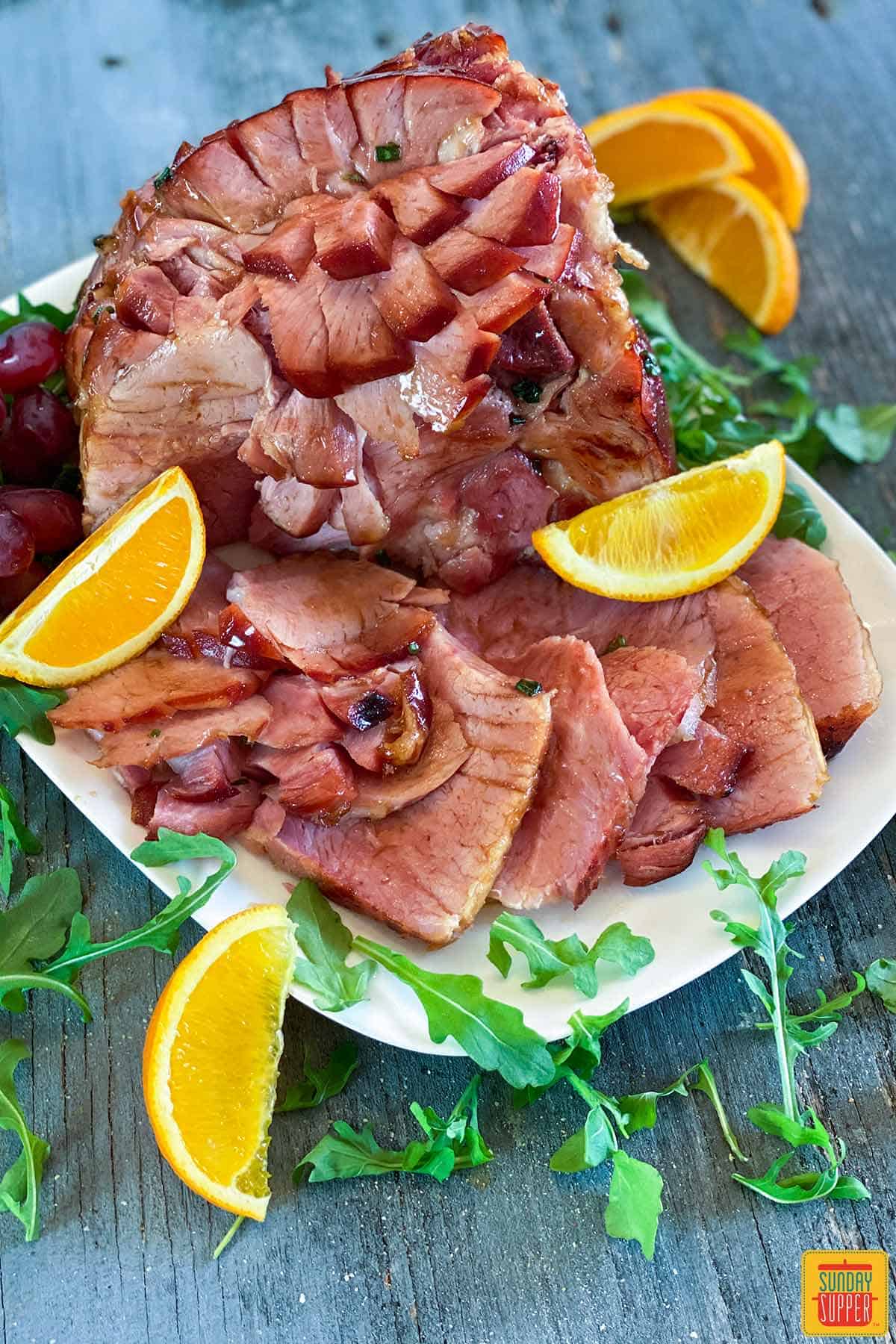 Instant pot ham with slices of orange and arugula on a platter
