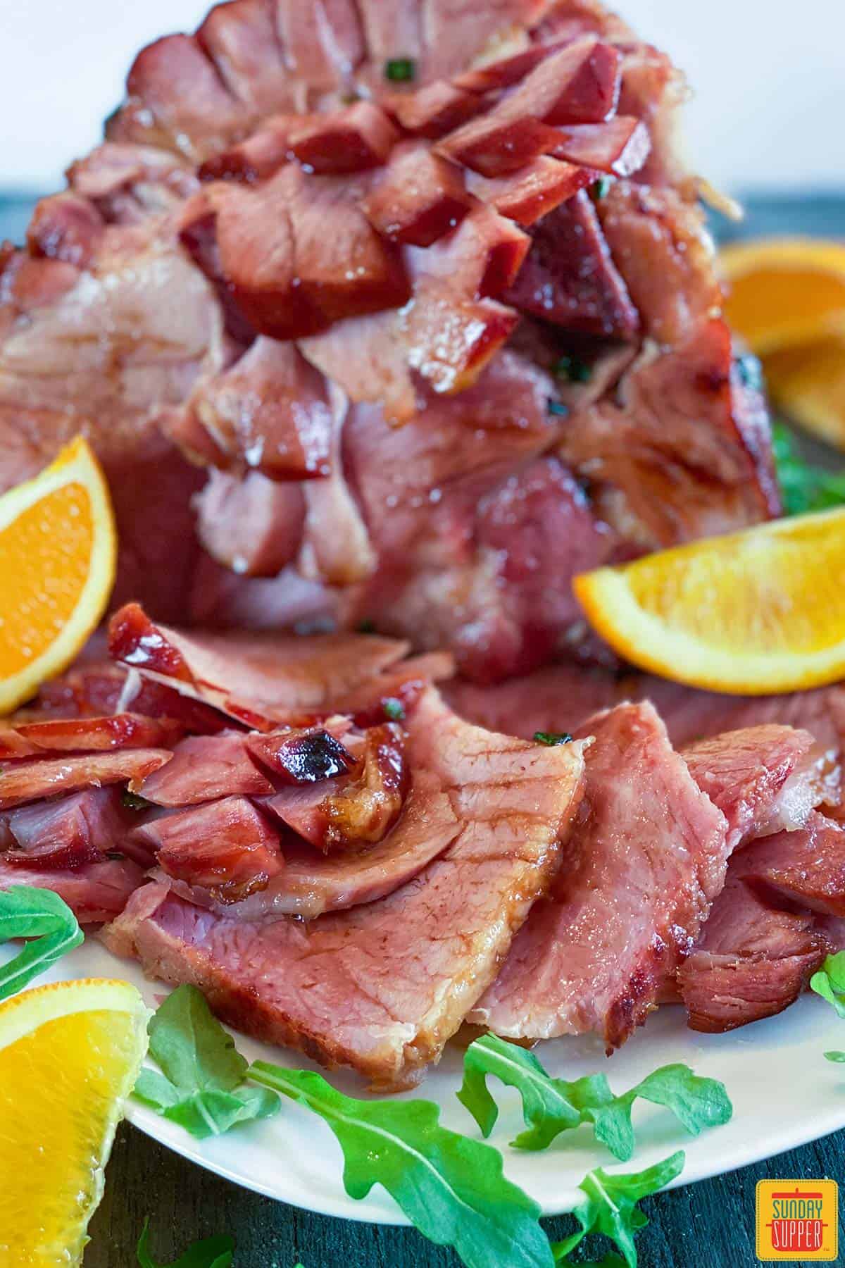 Close up of instant pot ham on a platter with orange slices and arugula