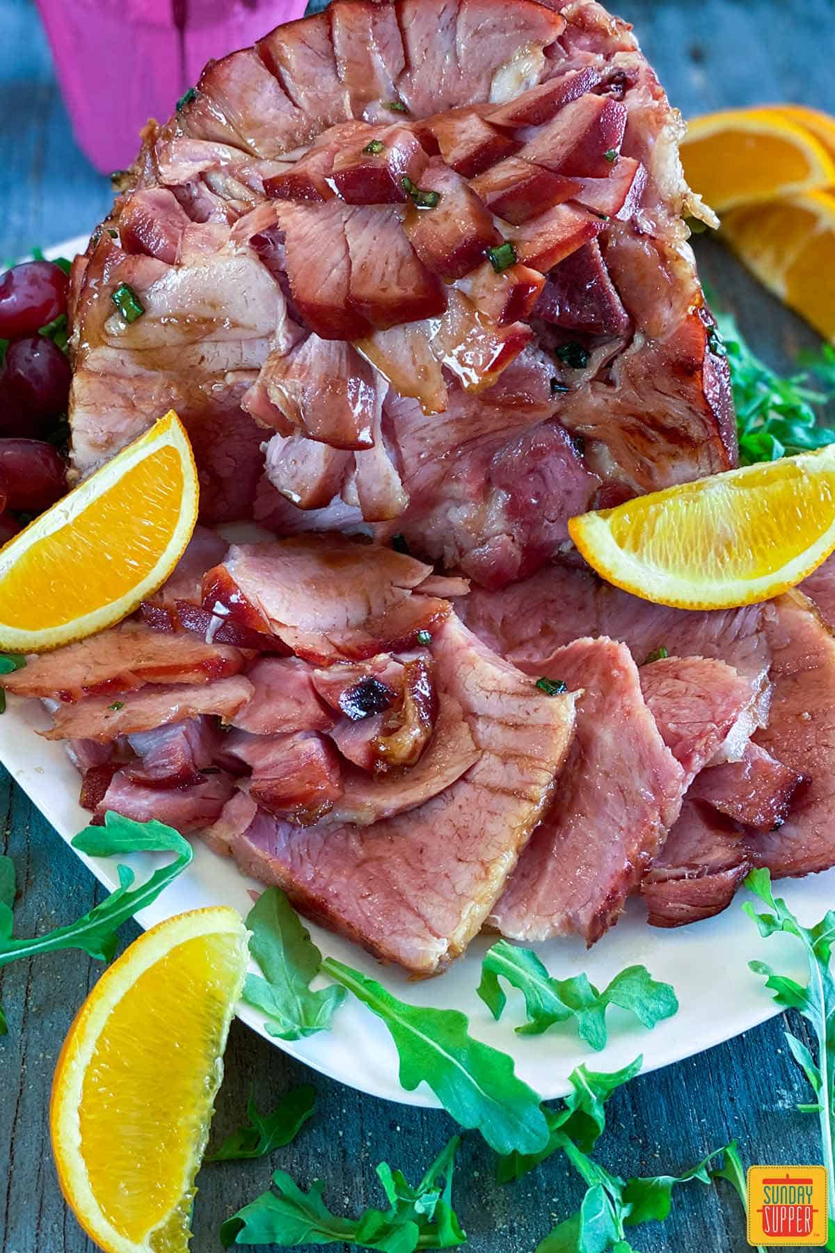 Ham on a platter with orange slices and arugula
