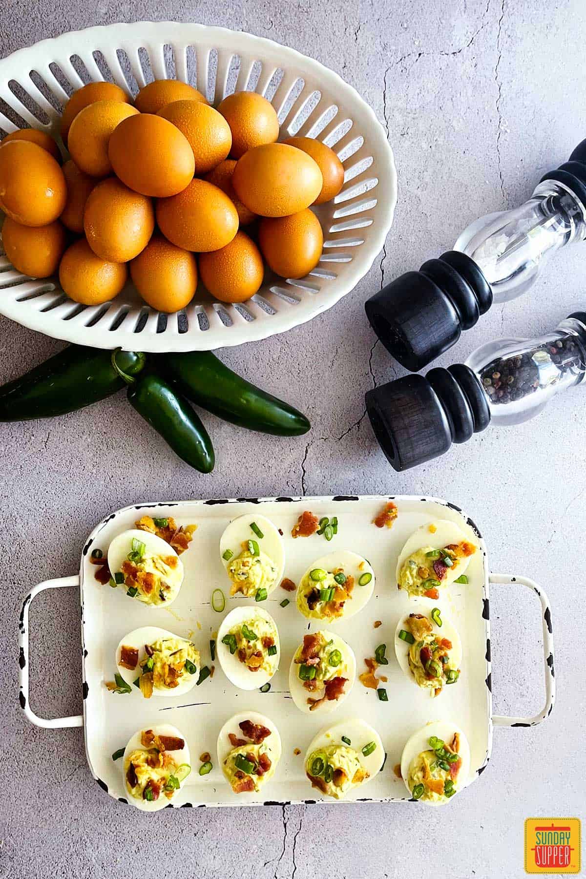 jalapeno popper deviled eggs with the ingredients to make them on a table