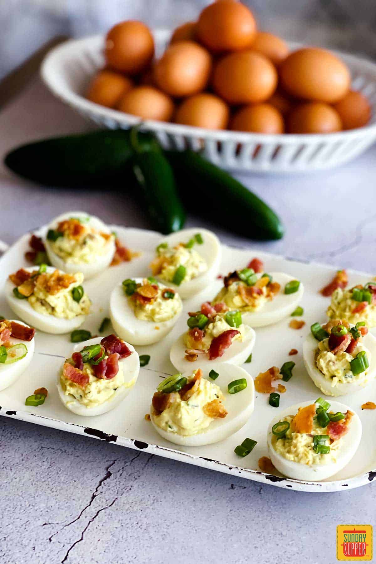 Jalapeno deviled eggs on a tray next to a bowl of eggs