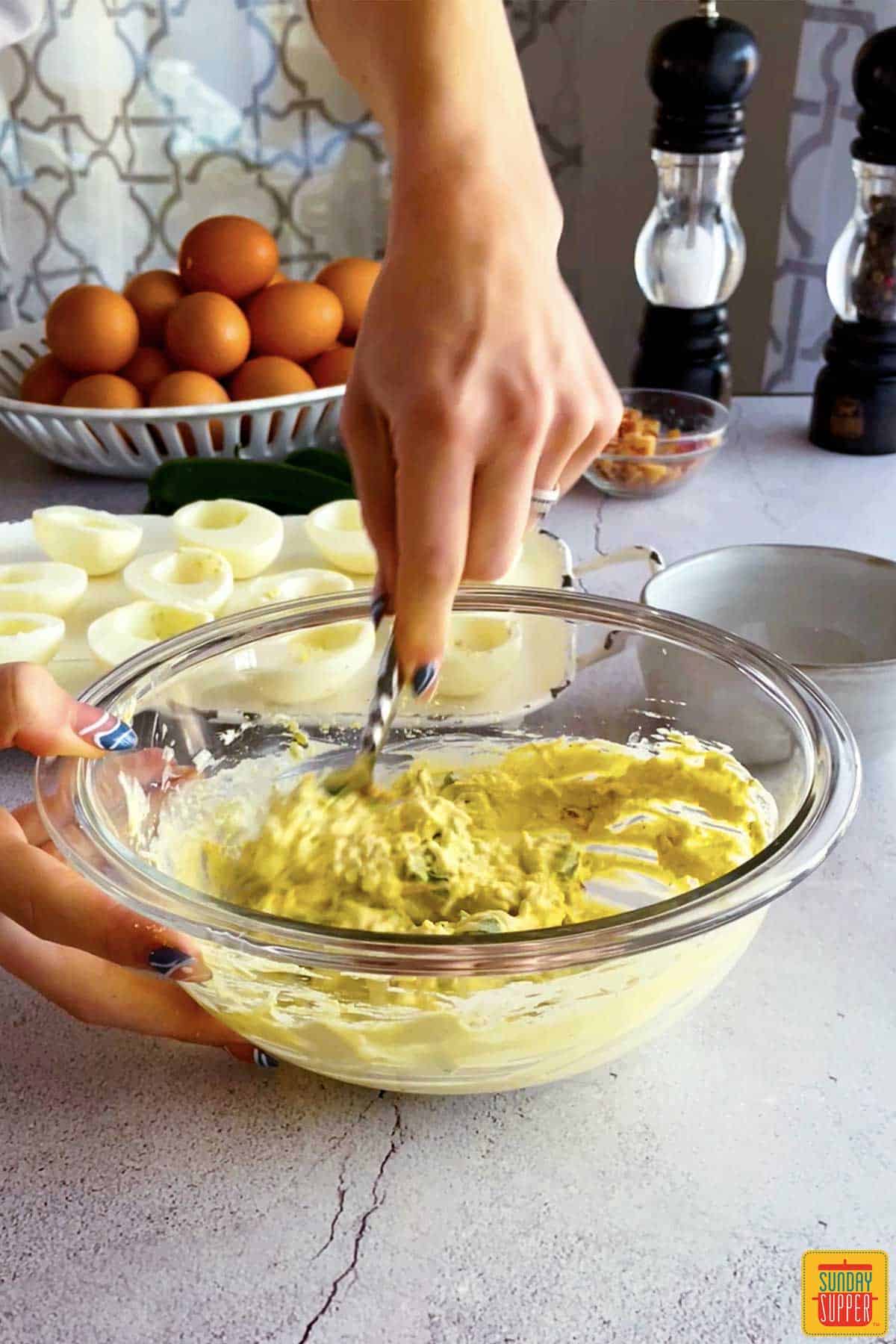 mashing jalapeno popper deviled egg ingredients in a bowl