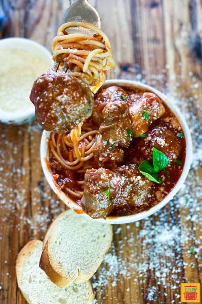 meatball on a fork over a bowl of meatballs with spaghetti