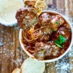 Lifting a meatball out of meatball sauce recipe over spaghetti in a white bowl